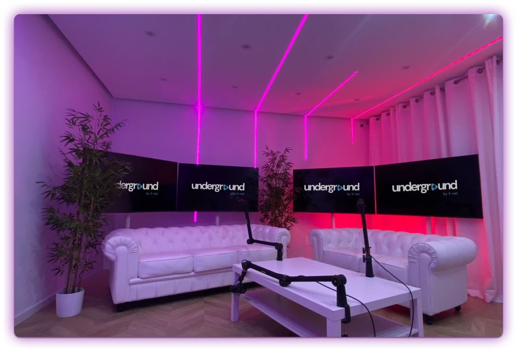 Plató con sofás blancos, pantallas negras e iluminación LED lineal amarilla y púrpura.